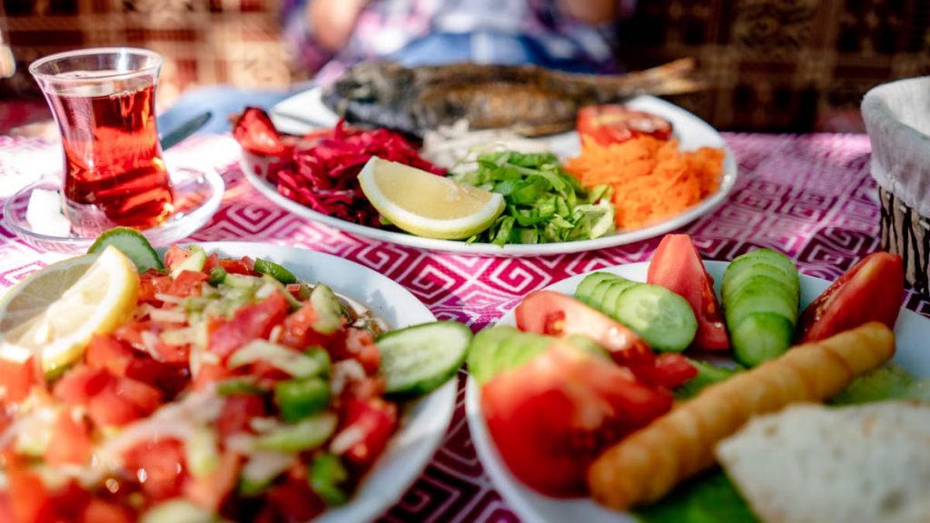 Close-up of a Mediterranean meal with grilled fish, fresh salad, and tea on a restaurant table.